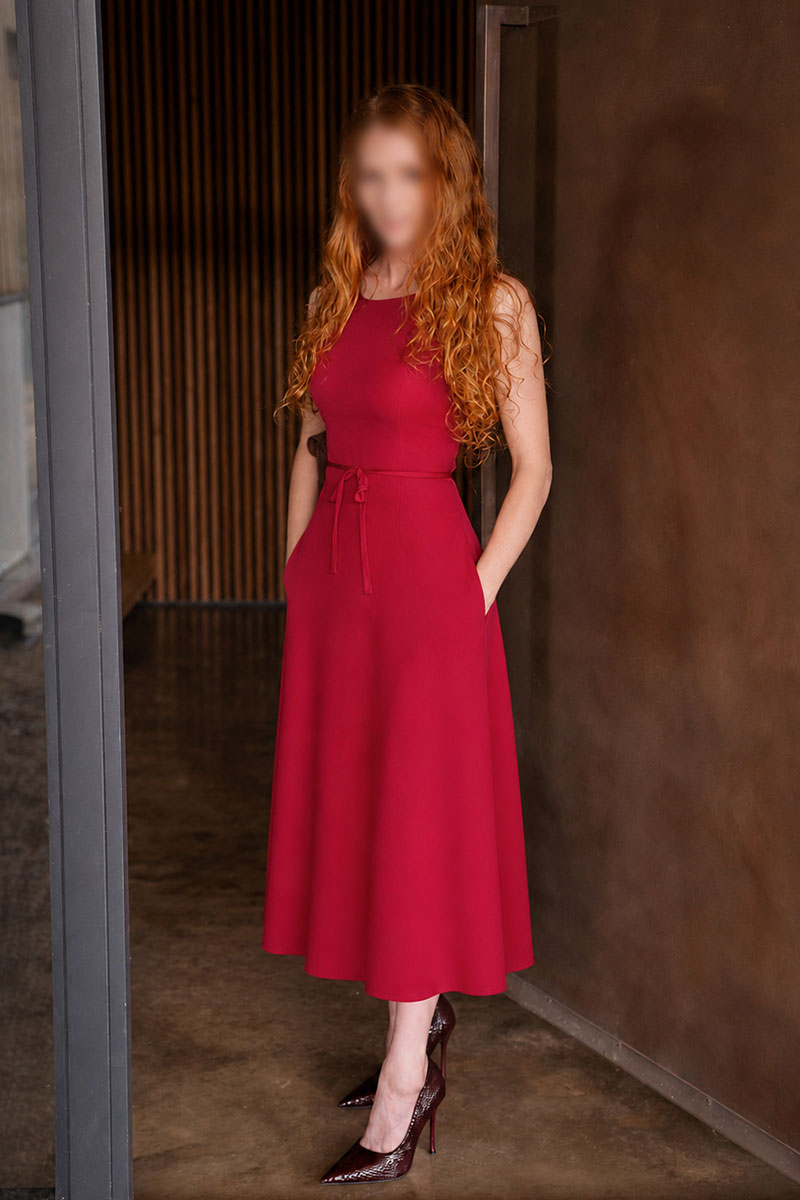 Lottie in a red midi dress and heels, standing in a doorway